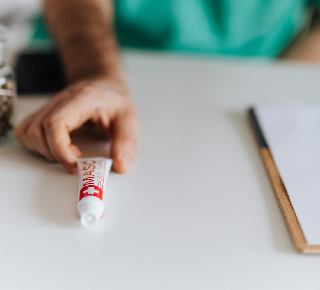 Person holding a tube of Savlon antiseptic cream on a white table.