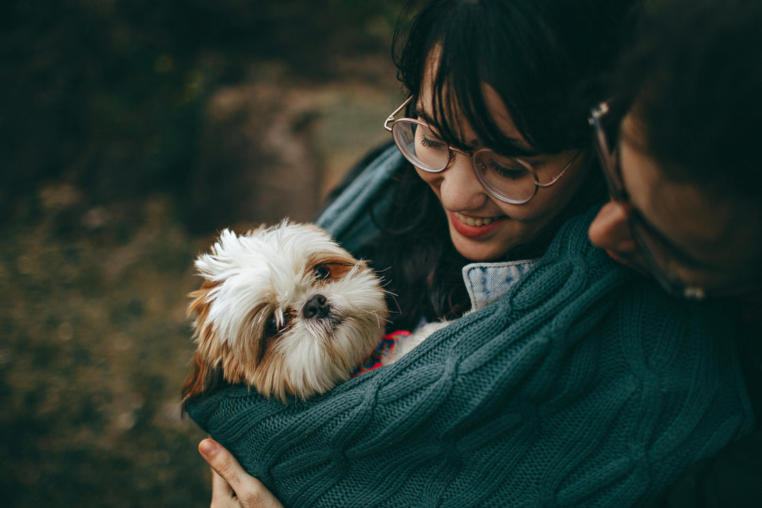 Woman holding a small white dog while smiling outdoors.