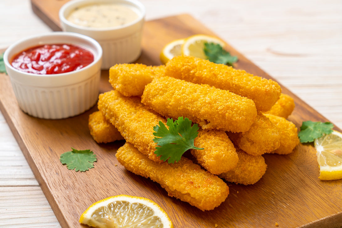 Breaded fish fingers served on a wooden board with lemon slices