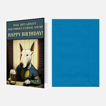 Bull Terrier birthday card featuring a Bull Terrier with tattoos, wearing a T-shirt, and drinking beer with 'Defy Gravity' birthday text. Blue envelope.