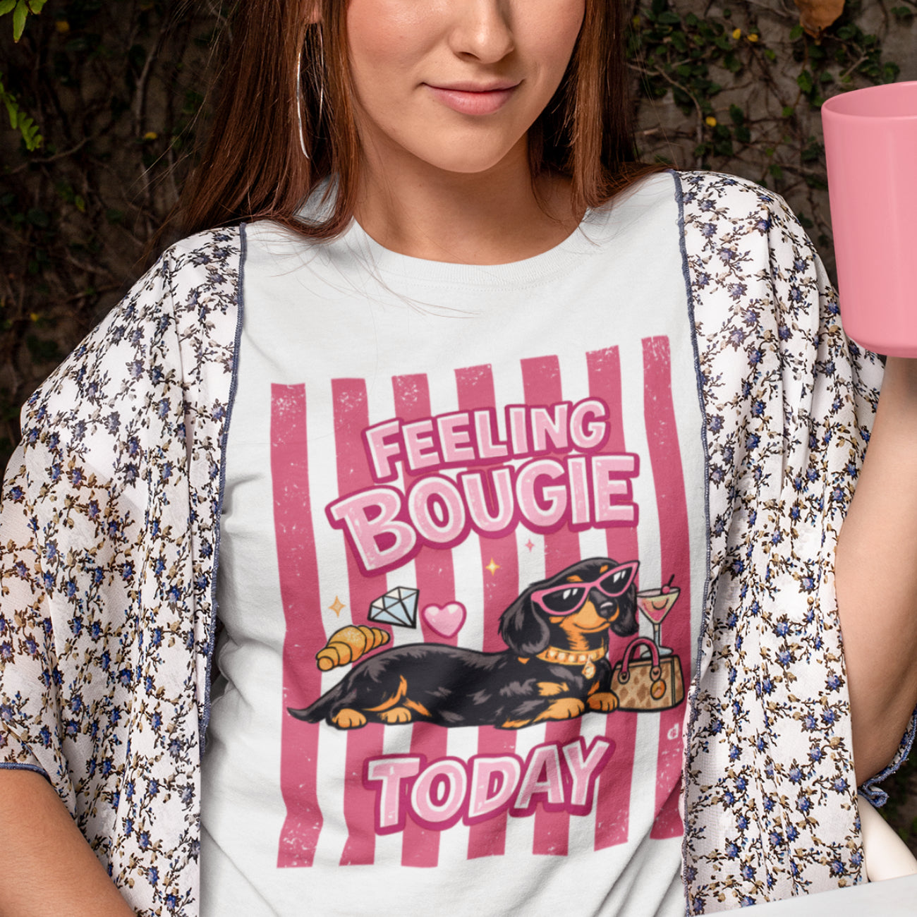 A woman wearing a white graphic t-shirt with a pink and black dachshund design that reads 'FEELING BOUGIE TODAY' and a matching floral kimono cardigan.
