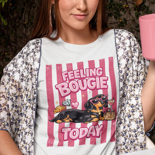 A woman wearing a white graphic t-shirt with a pink and black dachshund design that reads 'FEELING BOUGIE TODAY' and a matching floral kimono cardigan.