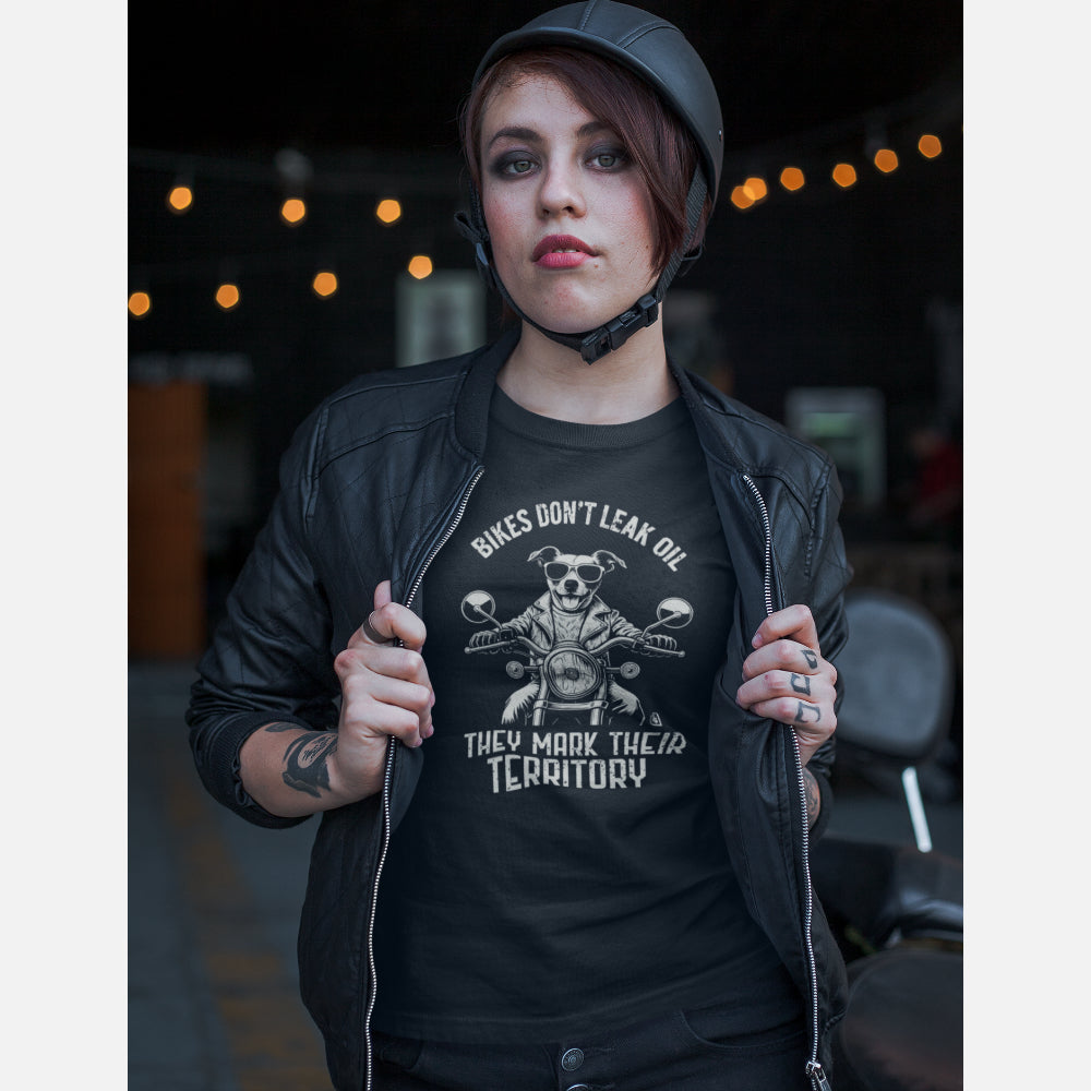 Women in a black T-shirt featuring a biker-style Jack Russell Terrier riding a motorcycle, wearing sunglasses and a leather jacket, with the slogan “Bikes Don’t Leak Oil, They Mark Their Territory” printed above and below the illustration in a vintage font.