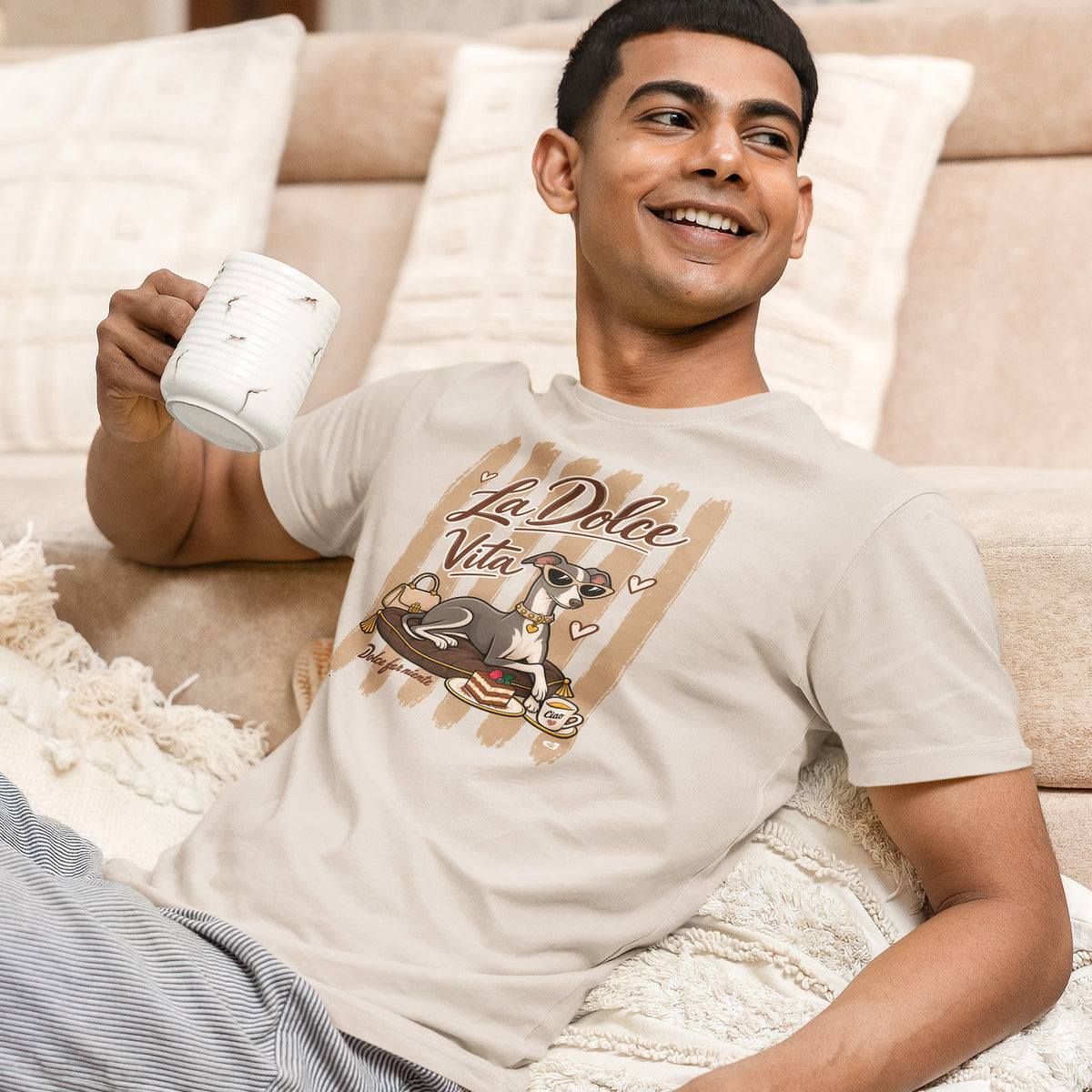 A man is wearing a Vintage White T-shirt featuring a graphic print of an Italian greyhound dog wearing sunglasses, sitting on a cushion with a cup of coffee, under the text 'La Dolce Vita'. 