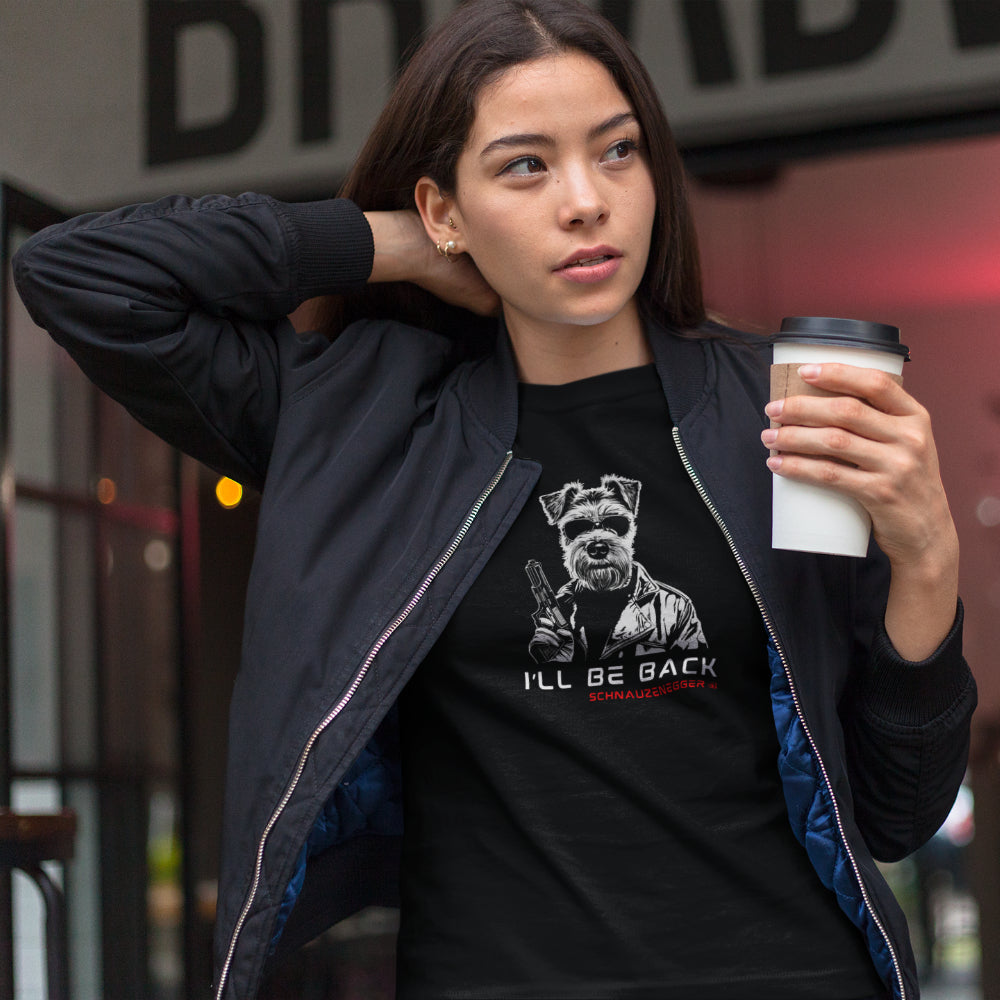 Woman in a b
lack T-shirt featuring a Miniature Schnauzer in Terminator style with sunglasses, leather jacket, and gun, slogan “I’LL BE BACK,” and text “SCHNAUZENEGGER.”