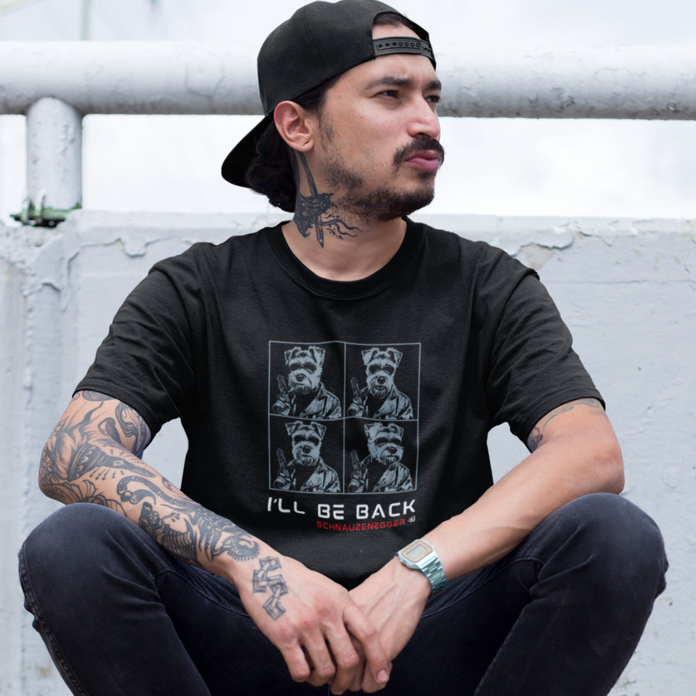 Man in a black unisex T-shirt with four-panel pop-art design in blue showing a Miniature Schnauzer in Terminator style with sunglasses, leather jacket, gun, slogan “I’LL BE BACK,” and text “SCHNAUZENEGGER.”