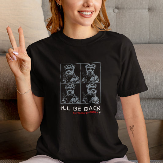 Women in a black unisex T-shirt with four-panel pop-art design in blue showing a Miniature Schnauzer in Terminator style with sunglasses, leather jacket, gun, slogan “I’LL BE BACK,” and text “SCHNAUZENEGGER.”