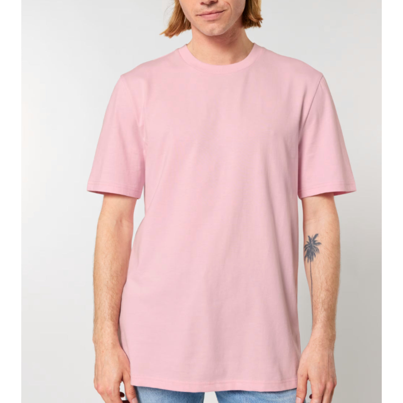 A person wearing a Stanley Stella cotton pink short-sleeve crewneck t-shirt, shown from the chin down against a light grey studio background.