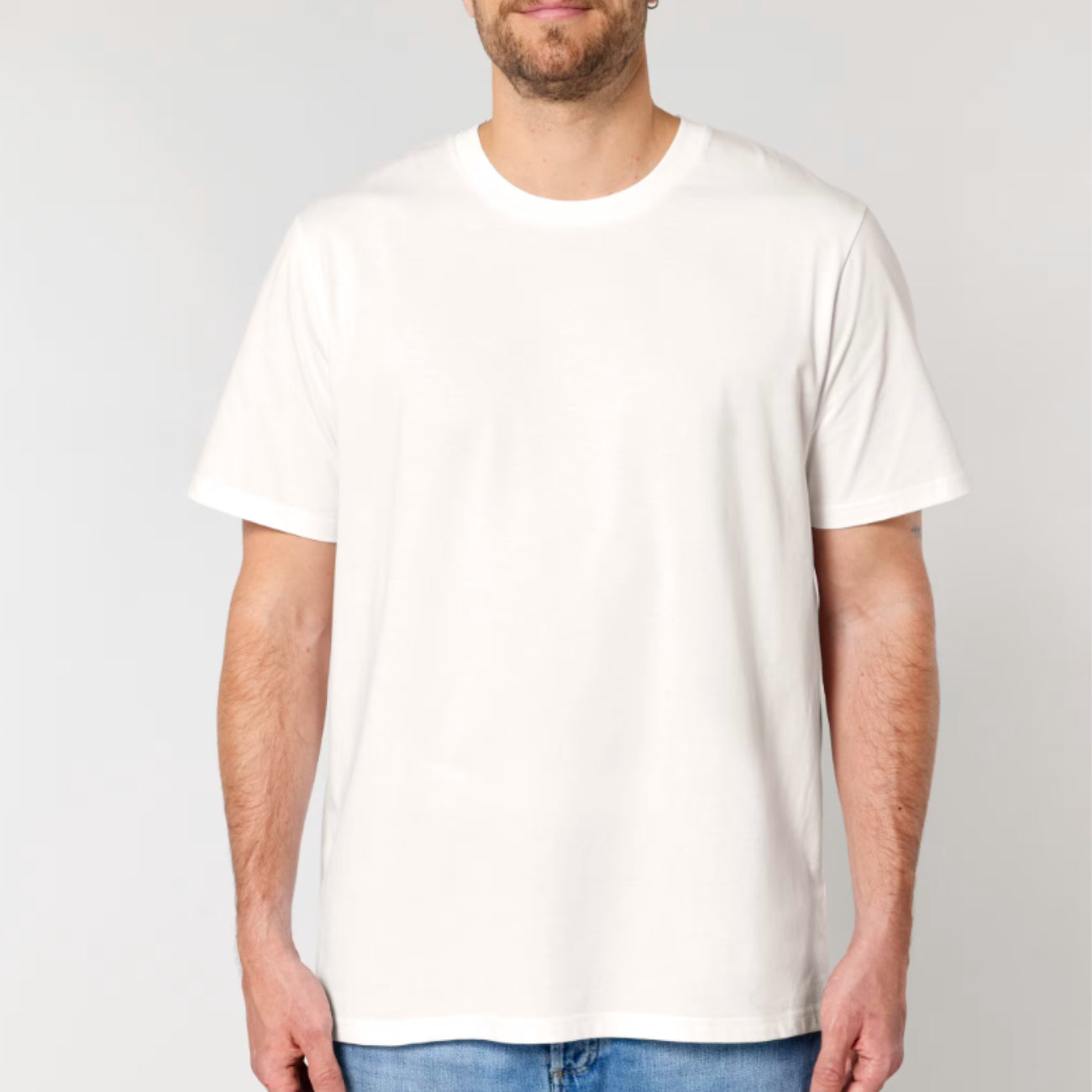 A man wearing a Stanley Stella off-white short-sleeve crewneck t-shirt, shown from the chin down against a light grey studio background.